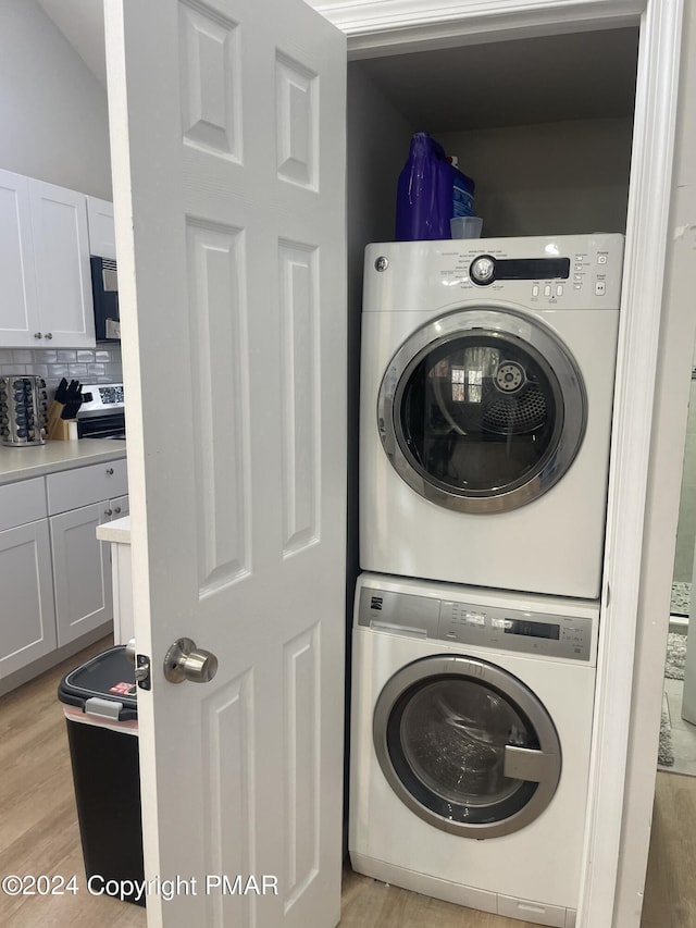 clothes washing area featuring laundry area, light wood-style flooring, and stacked washer and clothes dryer