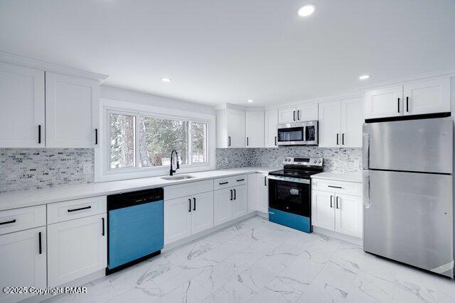 kitchen with a sink, stainless steel appliances, light countertops, white cabinets, and marble finish floor