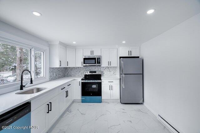 kitchen featuring marble finish floor, a sink, backsplash, stainless steel appliances, and baseboard heating