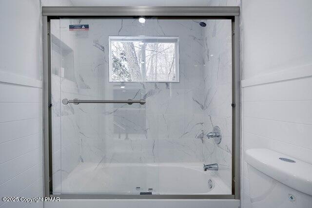 bathroom featuring enclosed tub / shower combo and toilet