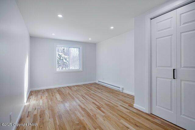 unfurnished bedroom featuring recessed lighting, light wood-style floors, baseboards, and a baseboard radiator