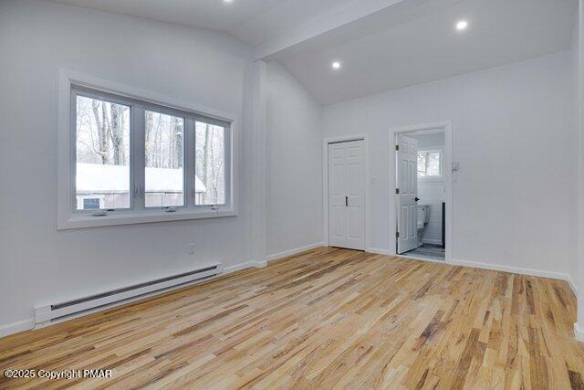 empty room featuring lofted ceiling with beams, a baseboard heating unit, baseboards, and wood finished floors