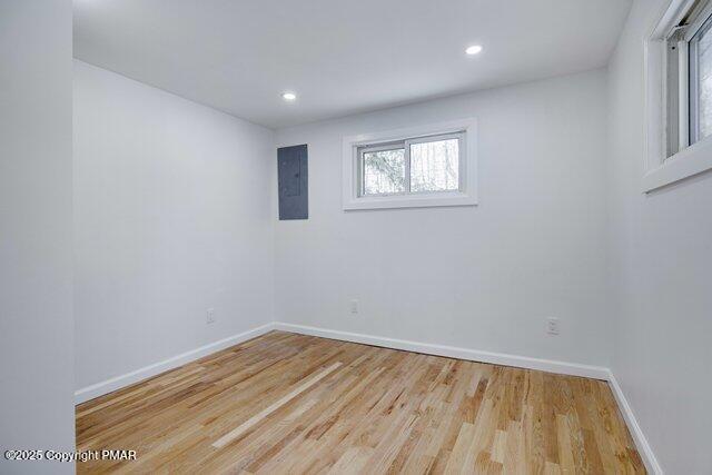 spare room with electric panel, recessed lighting, baseboards, and wood finished floors