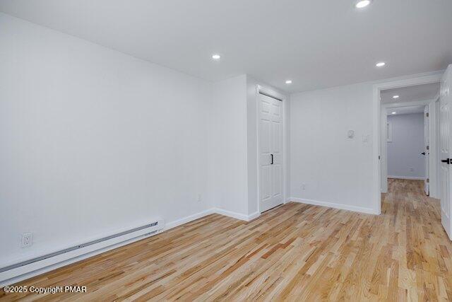 spare room featuring recessed lighting, baseboard heating, light wood-style flooring, and baseboards