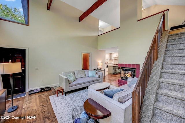 living room featuring wood finished floors, baseboards, a tile fireplace, stairs, and beamed ceiling