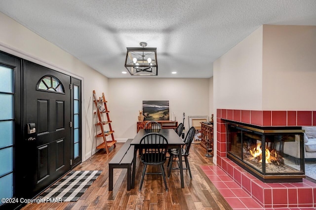 dining room with baseboards, a chandelier, a tile fireplace, wood finished floors, and a textured ceiling