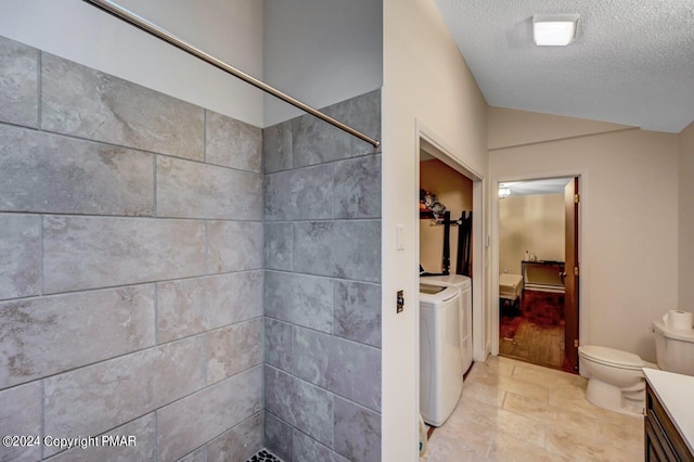 ensuite bathroom with toilet, lofted ceiling, tiled shower, independent washer and dryer, and a textured ceiling