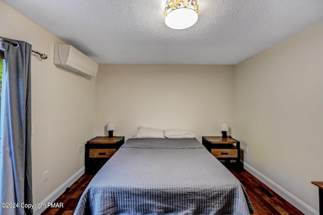 bedroom with a wall unit AC, wood finished floors, baseboards, and a textured ceiling