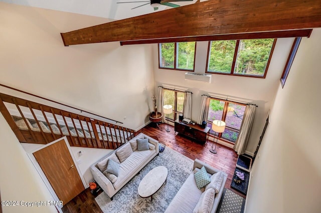 living area featuring beamed ceiling, a high ceiling, a ceiling fan, and wood finished floors