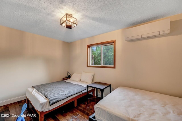 bedroom with a wall mounted air conditioner, baseboards, a textured ceiling, and hardwood / wood-style flooring