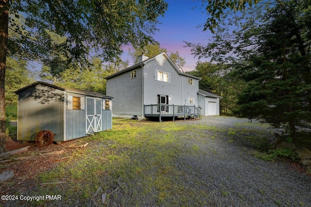 back of property at dusk with an outdoor structure, a storage unit, driveway, and a chimney