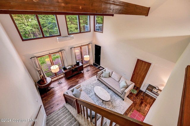 living room with beamed ceiling, an AC wall unit, a towering ceiling, and hardwood / wood-style floors