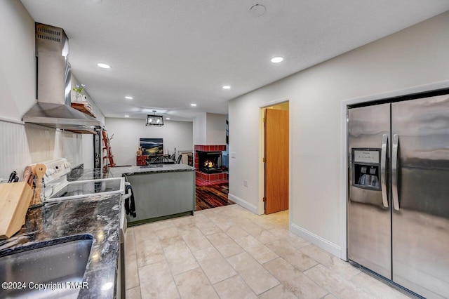 kitchen with wall chimney range hood, stainless steel fridge with ice dispenser, recessed lighting, a fireplace, and electric stove