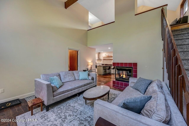 living room featuring beamed ceiling, wood finished floors, a fireplace, baseboards, and stairs