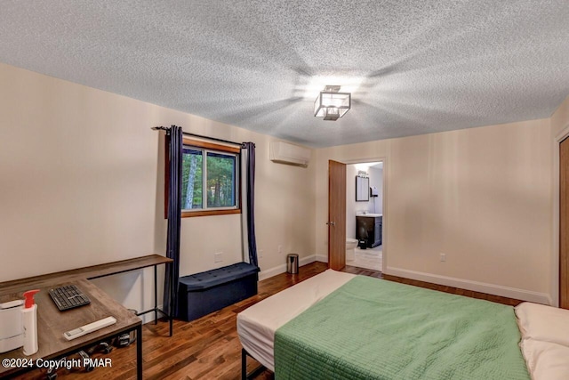 bedroom with an AC wall unit, a textured ceiling, wood finished floors, connected bathroom, and baseboards