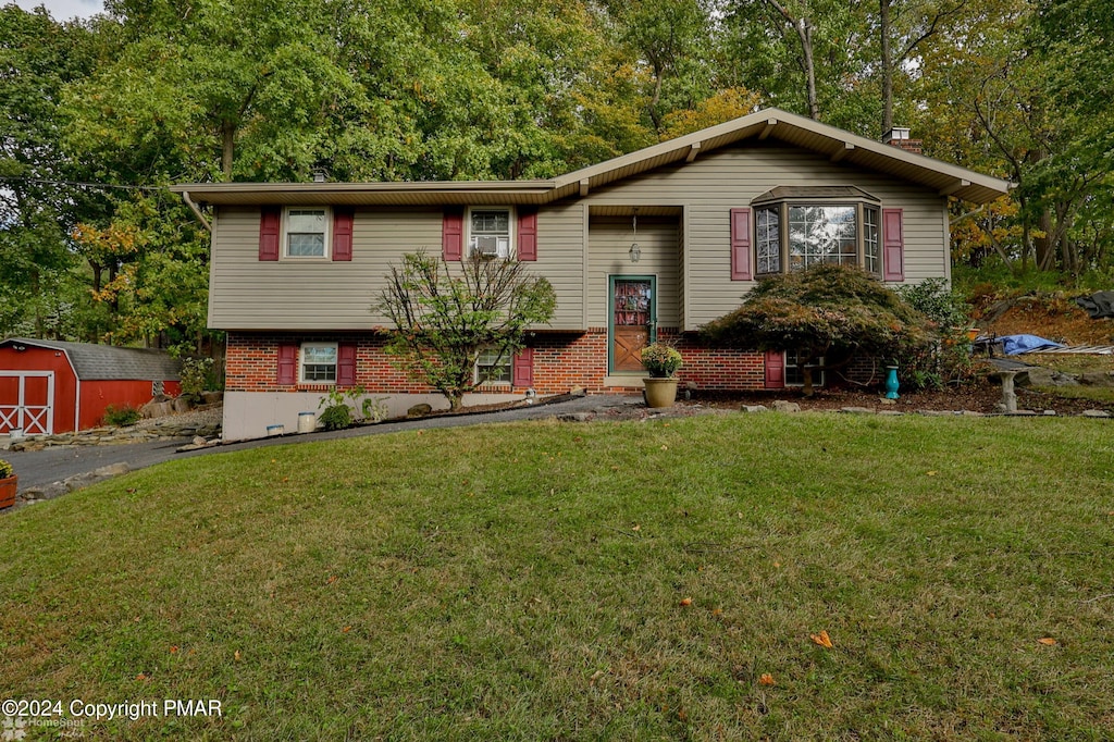 bi-level home featuring a front yard, brick siding, an outdoor structure, and a storage shed