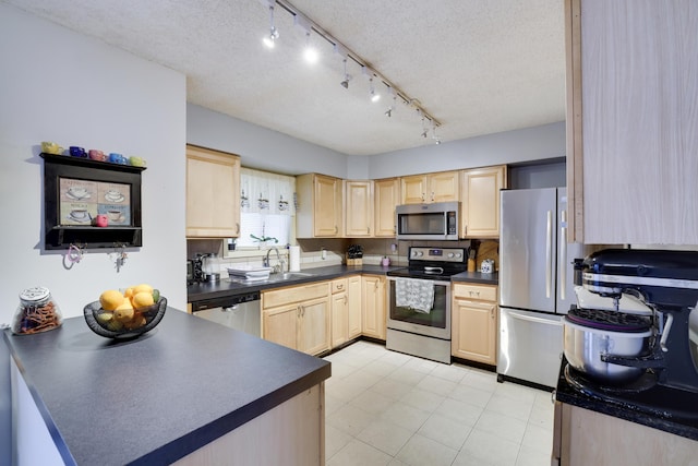 kitchen featuring dark countertops, light brown cabinets, a peninsula, stainless steel appliances, and a sink