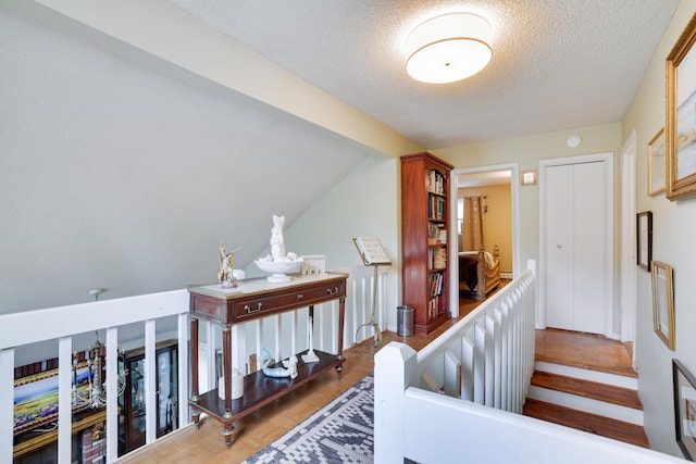 stairway featuring lofted ceiling, a textured ceiling, and wood finished floors