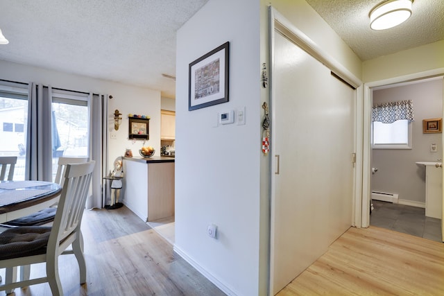 hall with baseboard heating, light wood-style flooring, a textured ceiling, and baseboards