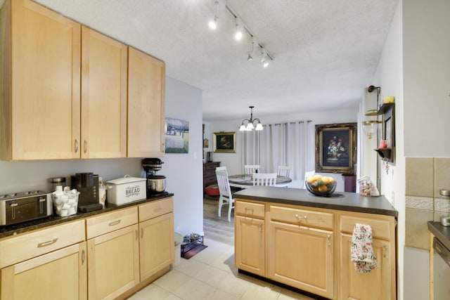 kitchen featuring dark countertops, light brown cabinets, a peninsula, an inviting chandelier, and a textured ceiling