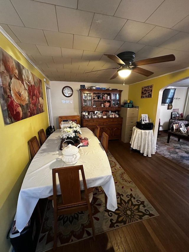 dining room with wood finished floors, a ceiling fan, and arched walkways