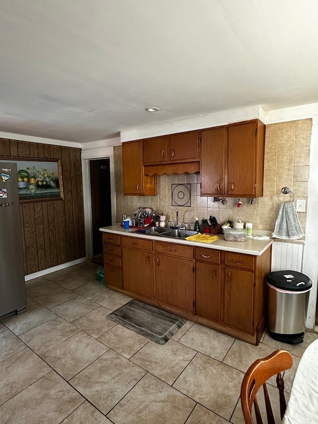 kitchen featuring freestanding refrigerator, light countertops, brown cabinetry, a sink, and decorative backsplash