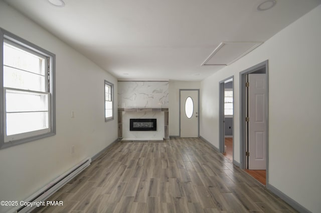 unfurnished living room with a baseboard radiator, a high end fireplace, and wood-type flooring