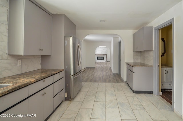 kitchen featuring gray cabinetry, backsplash, stainless steel refrigerator, and dark stone countertops