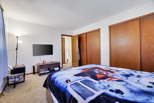 bedroom featuring light colored carpet, multiple closets, and baseboards