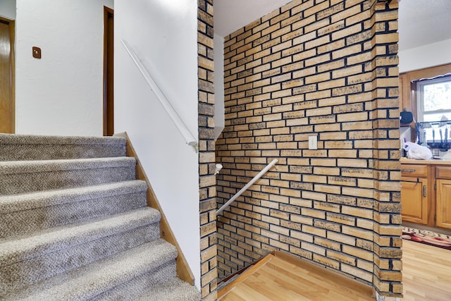 staircase featuring brick wall and wood finished floors