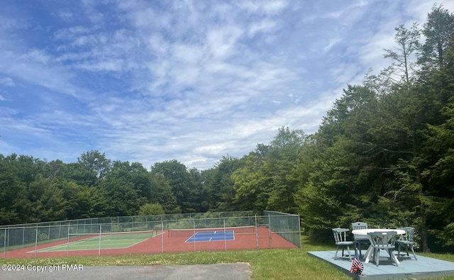 view of tennis court with fence and a forest view