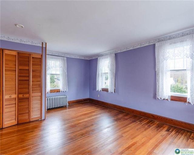 unfurnished bedroom featuring baseboards, radiator, a closet, and hardwood / wood-style flooring