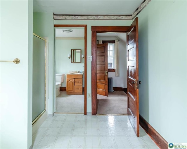 hall with baseboards, a sink, radiator, and light floors