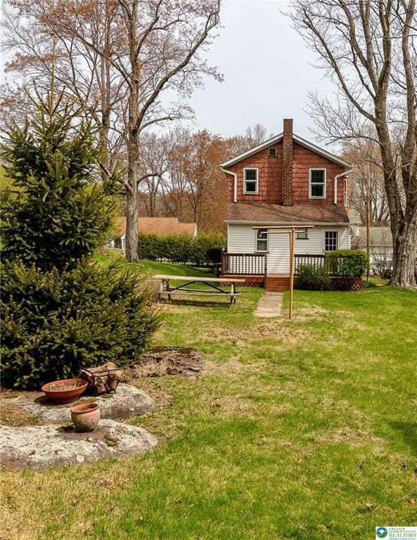 back of property featuring a wooden deck, a yard, and a chimney