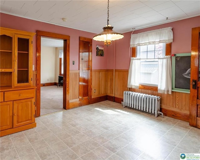 unfurnished dining area with wooden walls, baseboards, radiator, and a wainscoted wall