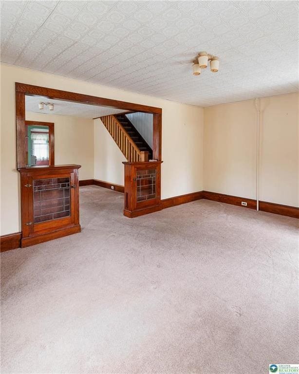 unfurnished living room featuring stairway, baseboards, and carpet flooring