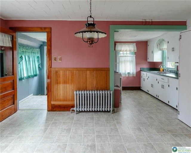 dining space with crown molding, light tile patterned floors, a wainscoted wall, wooden walls, and radiator heating unit