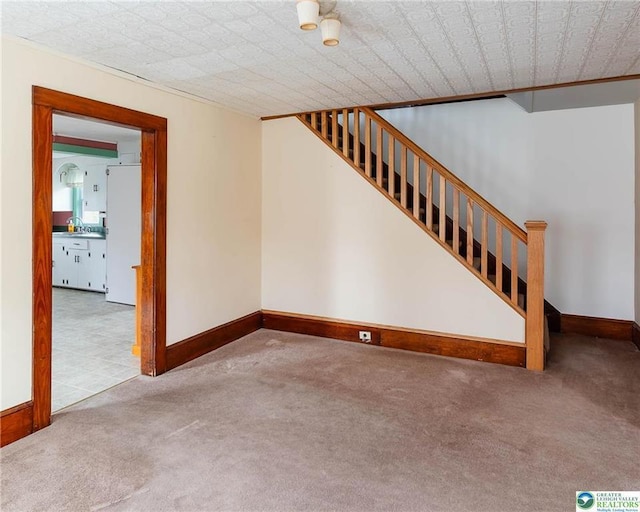 unfurnished living room featuring carpet floors, a sink, stairs, and baseboards