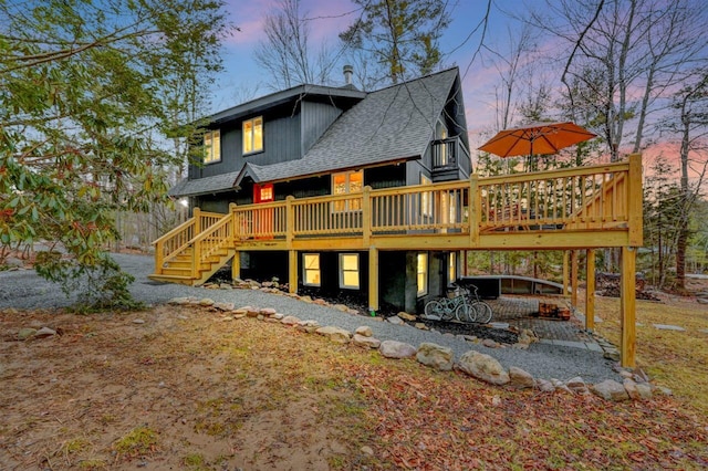 rear view of property with a shingled roof, stairway, and a wooden deck