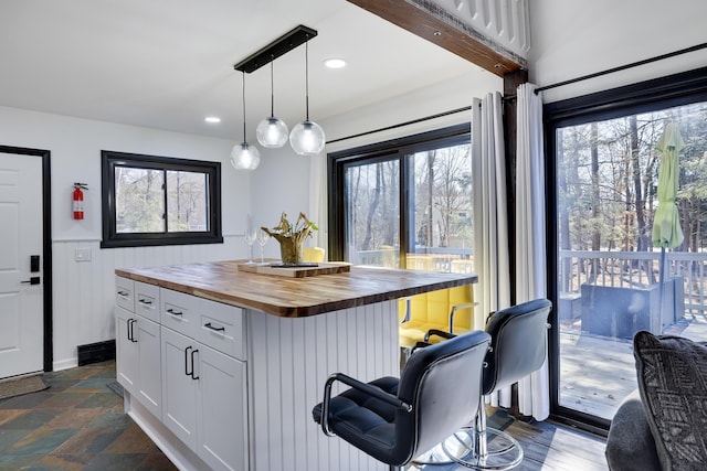 kitchen with a kitchen bar, a healthy amount of sunlight, white cabinetry, and butcher block counters