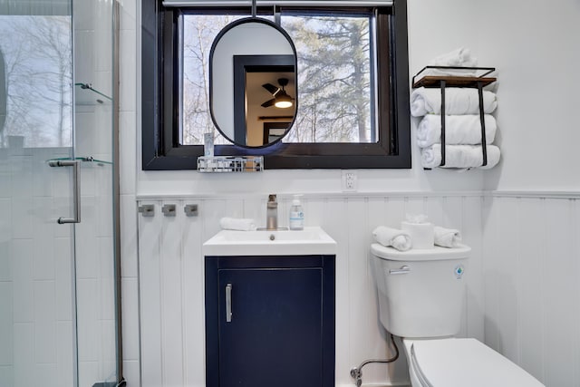 bathroom with vanity, toilet, a tile shower, and wainscoting