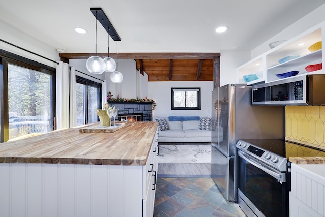 kitchen with butcher block countertops, open floor plan, appliances with stainless steel finishes, a stone fireplace, and white cabinets