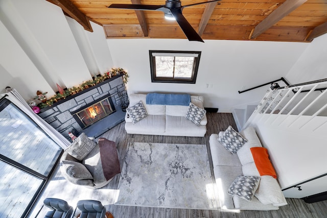 living area featuring vaulted ceiling with beams, a stone fireplace, and wood ceiling