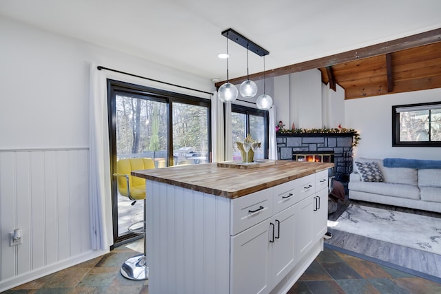 kitchen featuring stone tile floors, a stone fireplace, wooden counters, and lofted ceiling with beams