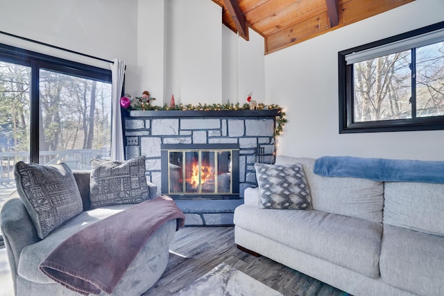 living area with a wealth of natural light, beamed ceiling, wood ceiling, and a stone fireplace