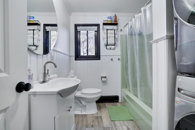 bathroom with crown molding, toilet, stacked washer and dryer, wainscoting, and wood finished floors