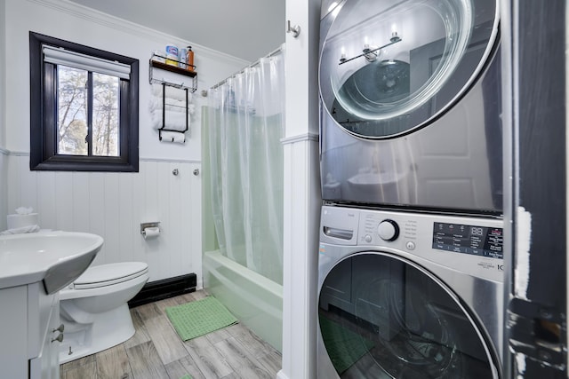 clothes washing area with ornamental molding, wood finished floors, wainscoting, stacked washer / dryer, and laundry area