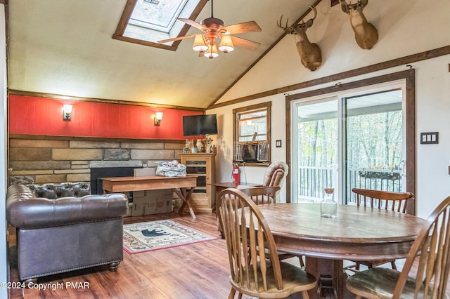 dining space with ceiling fan, lofted ceiling with skylight, a fireplace, and wood finished floors