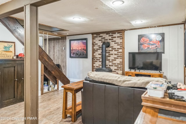 living area with light wood finished floors, a wood stove, wooden walls, a textured ceiling, and stairs