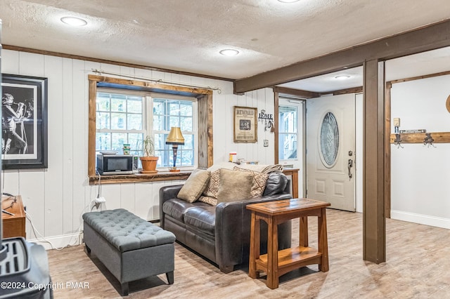 living area with light wood finished floors, beam ceiling, baseboards, and a textured ceiling